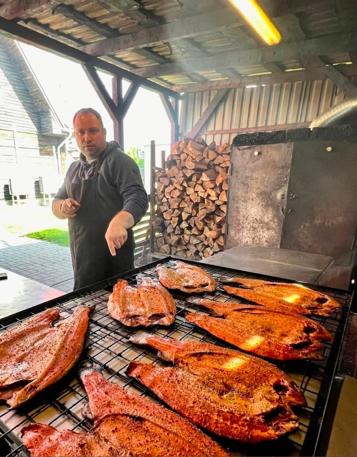 Tomas smoking fish beside a wood-fired smokehouse near Kaunas